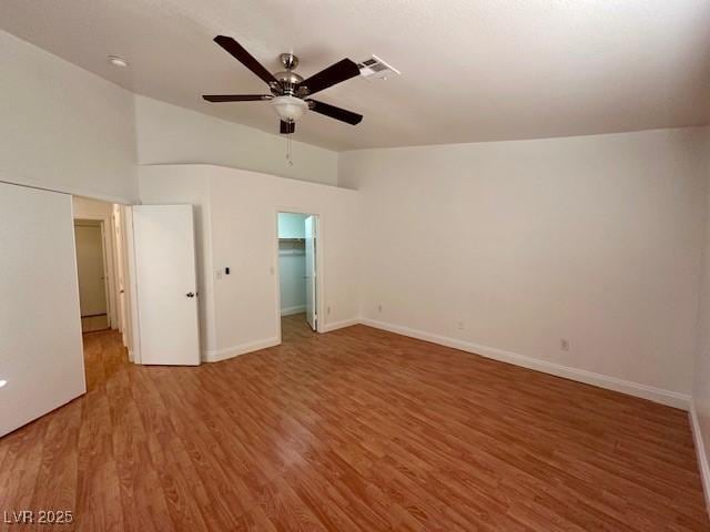 unfurnished bedroom with hardwood / wood-style flooring, a walk in closet, lofted ceiling, and ceiling fan