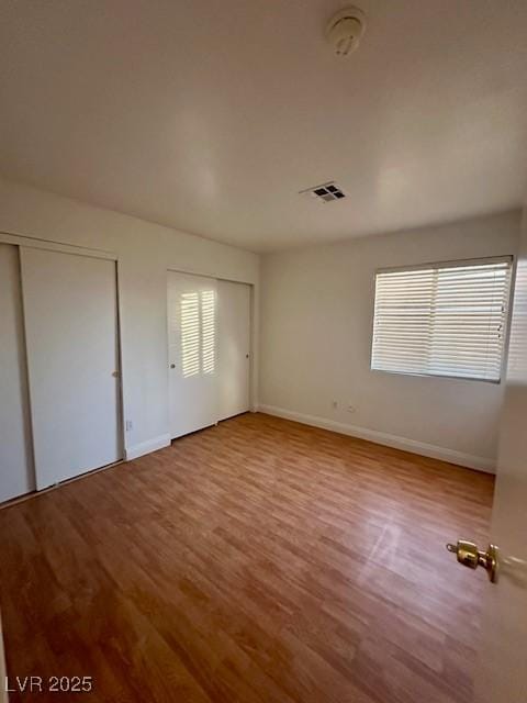 unfurnished bedroom with hardwood / wood-style floors and multiple closets