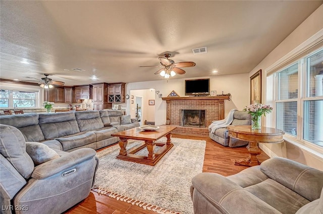 living room with a fireplace, light hardwood / wood-style flooring, and ceiling fan