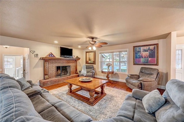 living room featuring ceiling fan, wood-type flooring, a brick fireplace, and plenty of natural light