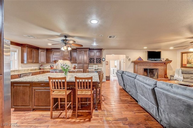 kitchen featuring dishwasher, ceiling fan, light stone counters, light hardwood / wood-style floors, and a kitchen bar