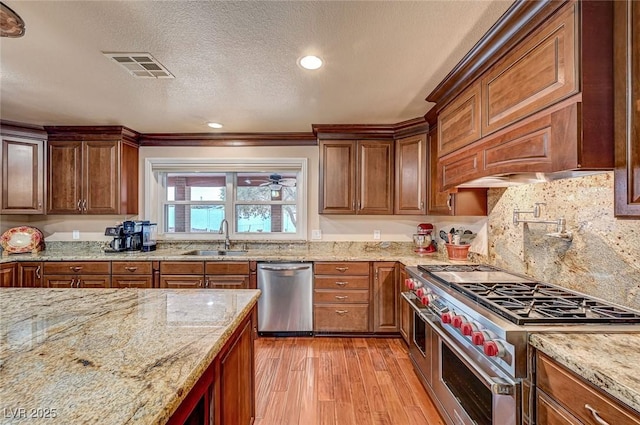 kitchen featuring stainless steel appliances, sink, light stone counters, and light hardwood / wood-style floors