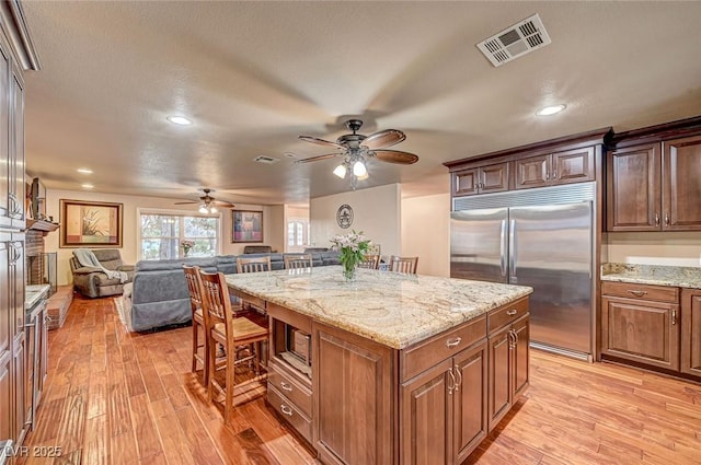 kitchen featuring light stone countertops, a kitchen island, built in appliances, and light wood-type flooring