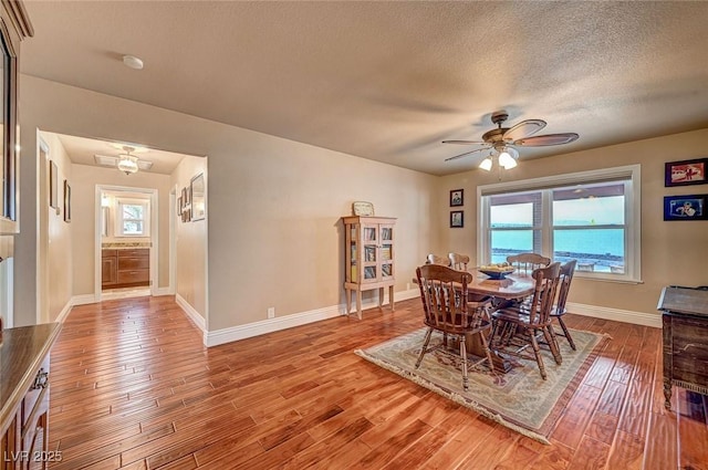 dining room with ceiling fan, light wood-type flooring, a textured ceiling, and a water view