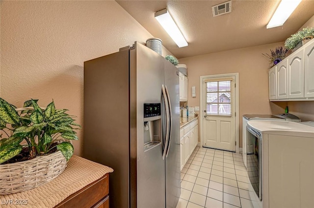 kitchen with stainless steel refrigerator with ice dispenser, white cabinetry, a textured ceiling, light tile patterned floors, and independent washer and dryer