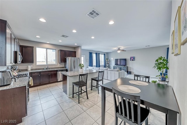 kitchen with light tile patterned flooring, sink, a center island, stainless steel appliances, and light stone countertops