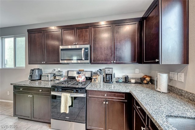 kitchen featuring appliances with stainless steel finishes, sink, light tile patterned floors, light stone countertops, and dark brown cabinets