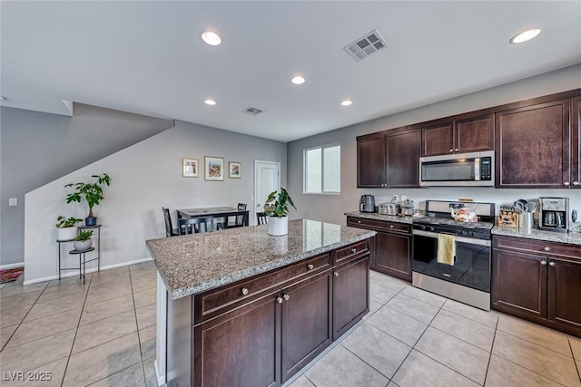 kitchen with appliances with stainless steel finishes, light stone countertops, a kitchen island, and light tile patterned floors