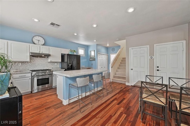 kitchen featuring a breakfast bar, a center island, stainless steel range, white cabinets, and black fridge