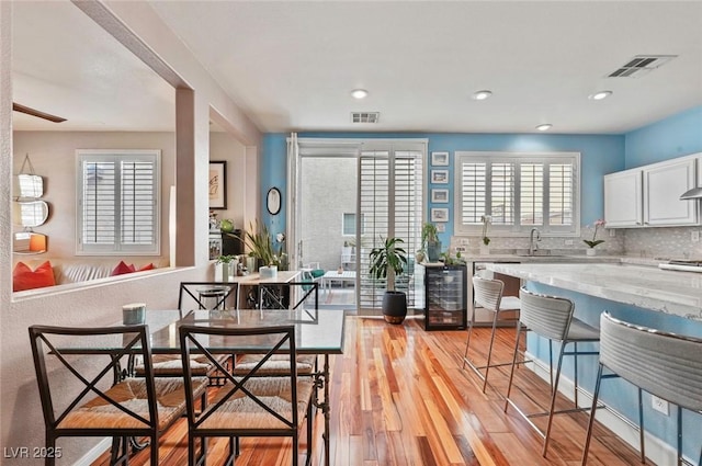 kitchen featuring sink, light hardwood / wood-style flooring, dishwasher, tasteful backsplash, and white cabinets