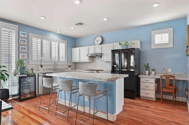 kitchen featuring light hardwood / wood-style floors, white cabinets, a kitchen island, stainless steel dishwasher, and black fridge