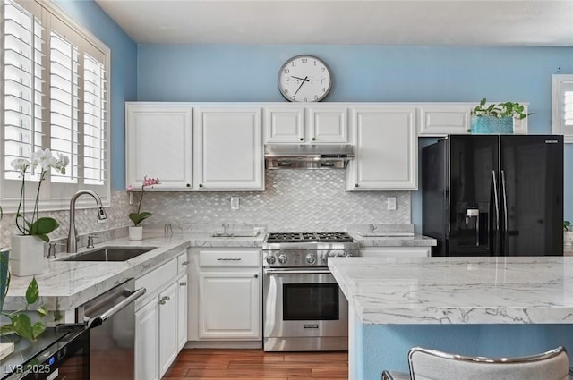 kitchen with sink, white cabinetry, appliances with stainless steel finishes, hardwood / wood-style floors, and backsplash