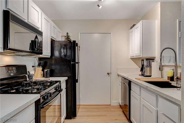 kitchen featuring white cabinetry, sink, black appliances, and light wood-type flooring