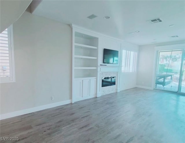 unfurnished living room featuring visible vents, baseboards, wood finished floors, and a glass covered fireplace