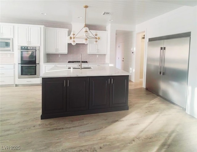 kitchen with tasteful backsplash, visible vents, white cabinets, light wood-style flooring, and built in appliances