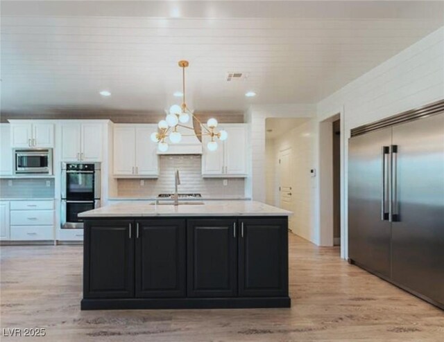 kitchen with built in appliances, pendant lighting, an island with sink, and white cabinets