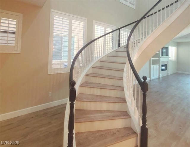 staircase featuring a fireplace, baseboards, and wood finished floors