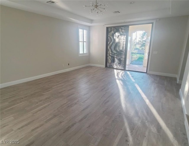 unfurnished room with wood-type flooring, a raised ceiling, and a chandelier