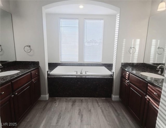 bathroom with hardwood / wood-style floors, vanity, and tiled bath