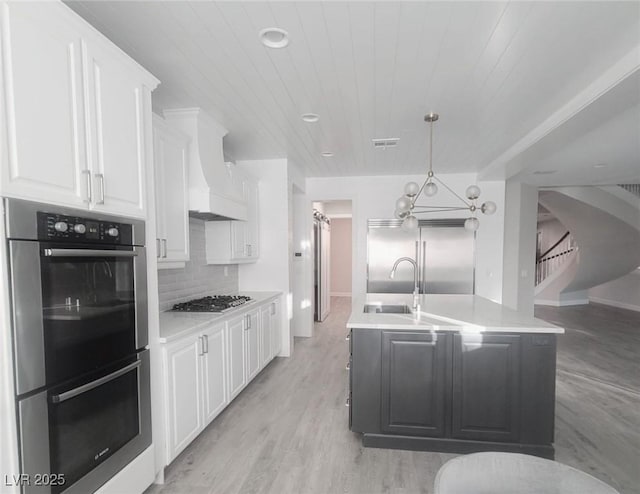 kitchen with premium range hood, appliances with stainless steel finishes, decorative backsplash, white cabinets, and decorative light fixtures