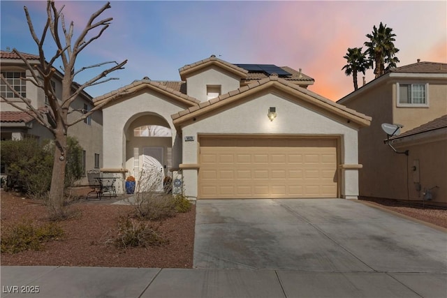 mediterranean / spanish home with a garage, solar panels, a tiled roof, driveway, and stucco siding