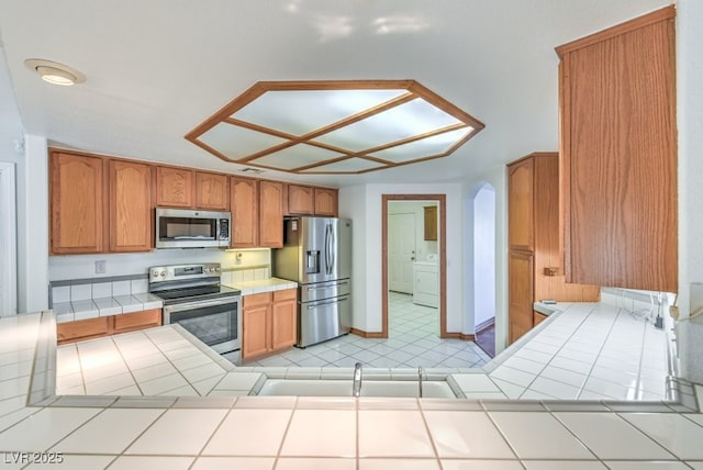 kitchen with appliances with stainless steel finishes, sink, tile counters, independent washer and dryer, and kitchen peninsula