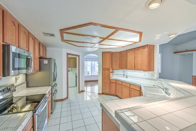 kitchen featuring appliances with stainless steel finishes, tile counters, kitchen peninsula, and sink