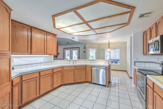 kitchen with tile countertops, sink, hanging light fixtures, kitchen peninsula, and stainless steel appliances