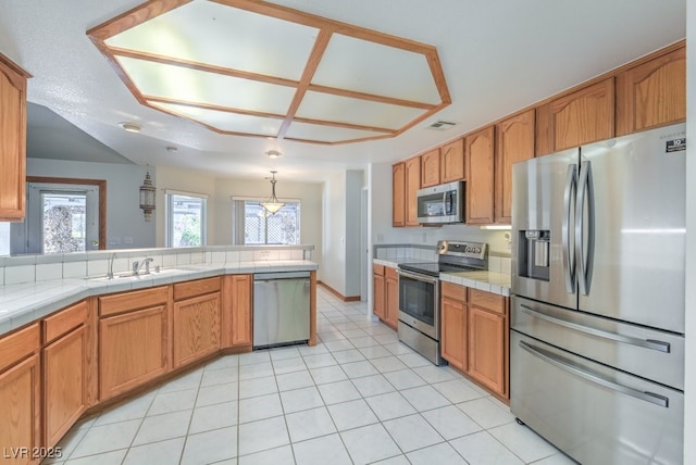 kitchen with sink, light tile patterned floors, stainless steel appliances, tile counters, and decorative light fixtures