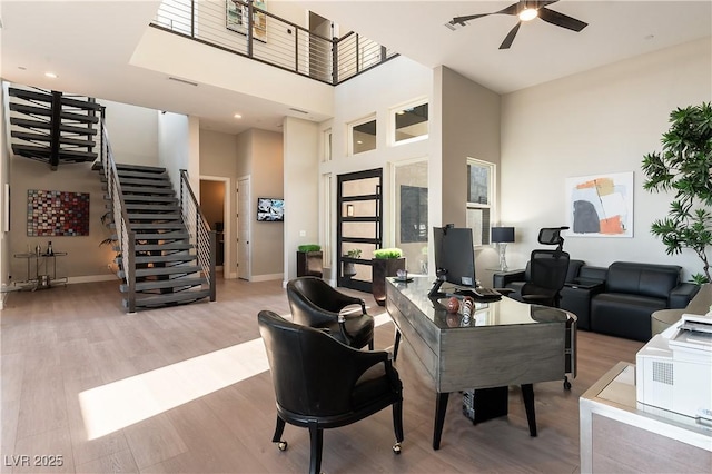 living room featuring ceiling fan, a towering ceiling, and light hardwood / wood-style floors