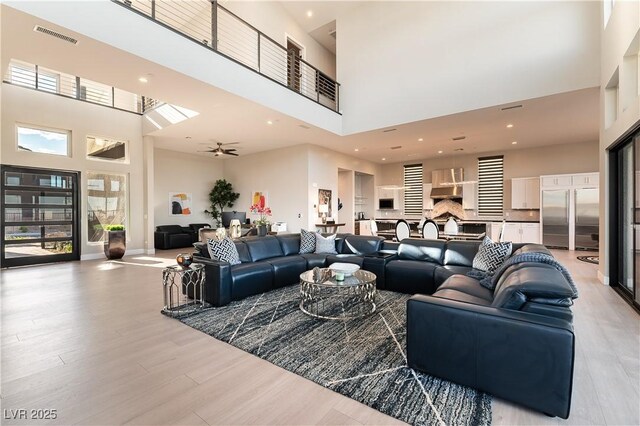 living room featuring a towering ceiling, ceiling fan, and light wood-type flooring