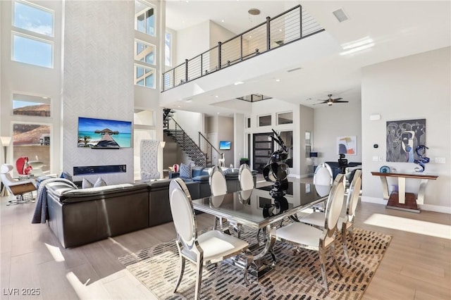 dining space with a fireplace, wood-type flooring, ceiling fan, and a high ceiling