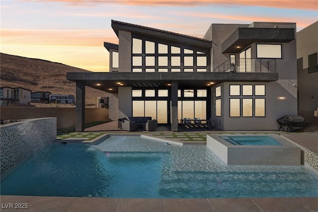 back house at dusk with a patio, a balcony, and a pool with hot tub