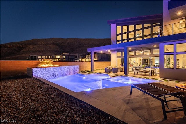 pool at twilight with a mountain view, an outdoor living space with a fire pit, a patio, and an in ground hot tub