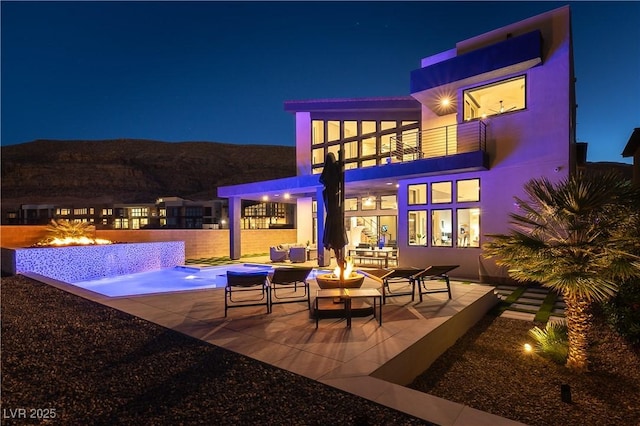 patio at twilight featuring a balcony, an outdoor fire pit, and a mountain view