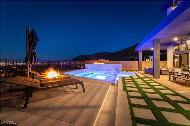 pool at night with an in ground hot tub, a mountain view, a patio, and an outdoor living space with a fire pit