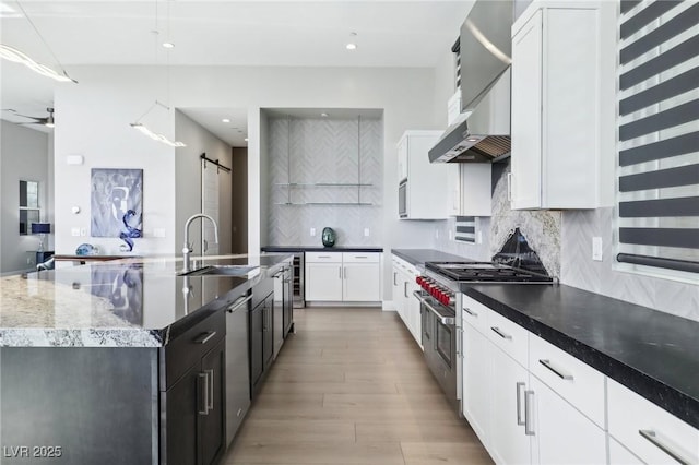 kitchen featuring white cabinets, stainless steel appliances, a barn door, and an island with sink