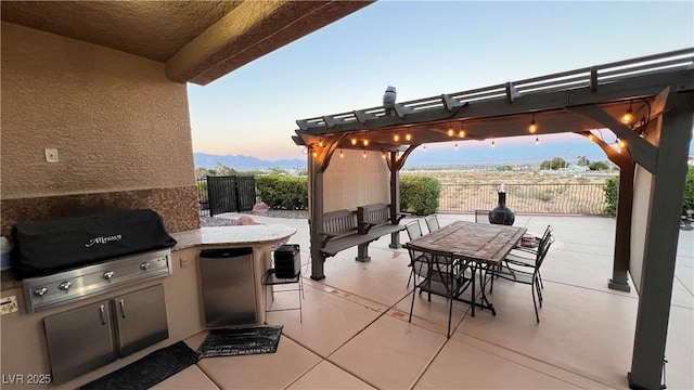 patio terrace at dusk with an outdoor kitchen, grilling area, and a pergola