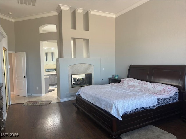 bedroom featuring connected bathroom, crown molding, wood-type flooring, and a multi sided fireplace