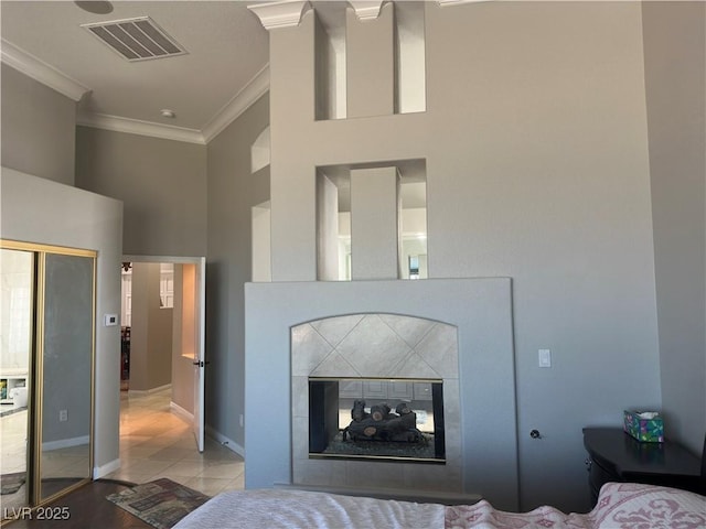 bedroom featuring a towering ceiling, a tiled fireplace, light tile patterned floors, crown molding, and a closet