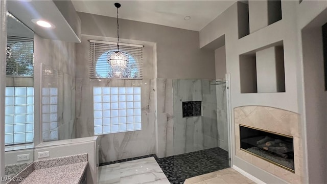 bathroom with a tile shower, vanity, a notable chandelier, and a premium fireplace