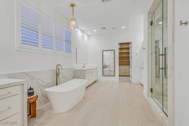 full bath featuring a stall shower, visible vents, wood finished floors, a freestanding bath, and vanity