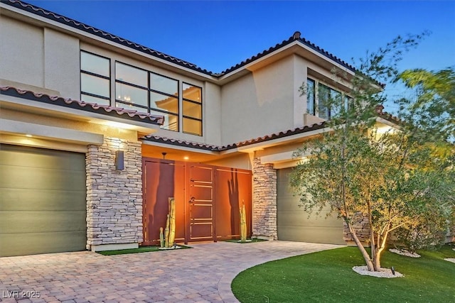 view of front of property with stone siding, a tile roof, an attached garage, and stucco siding