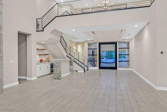 foyer with light wood finished floors, an inviting chandelier, beverage cooler, baseboards, and stairs