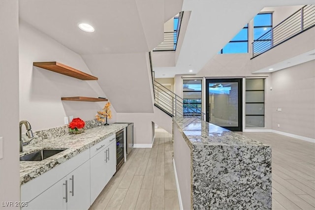 kitchen featuring light stone counters, open shelves, white cabinets, a sink, and light wood-type flooring