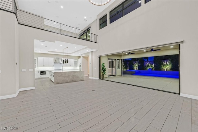 unfurnished living room with light wood-type flooring, a towering ceiling, baseboards, and recessed lighting