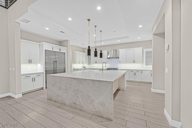 kitchen with a large island, recessed lighting, stainless steel built in fridge, a sink, and wall chimney range hood