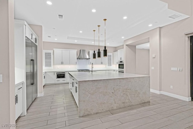 kitchen with a spacious island, wall chimney exhaust hood, appliances with stainless steel finishes, wood tiled floor, and recessed lighting