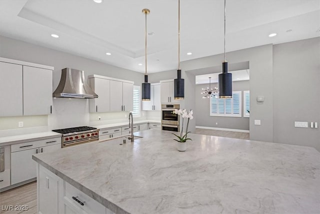 kitchen featuring recessed lighting, a raised ceiling, a sink, and wall chimney range hood