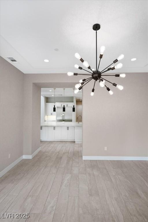 unfurnished living room featuring visible vents, light wood-style flooring, baseboards, and an inviting chandelier